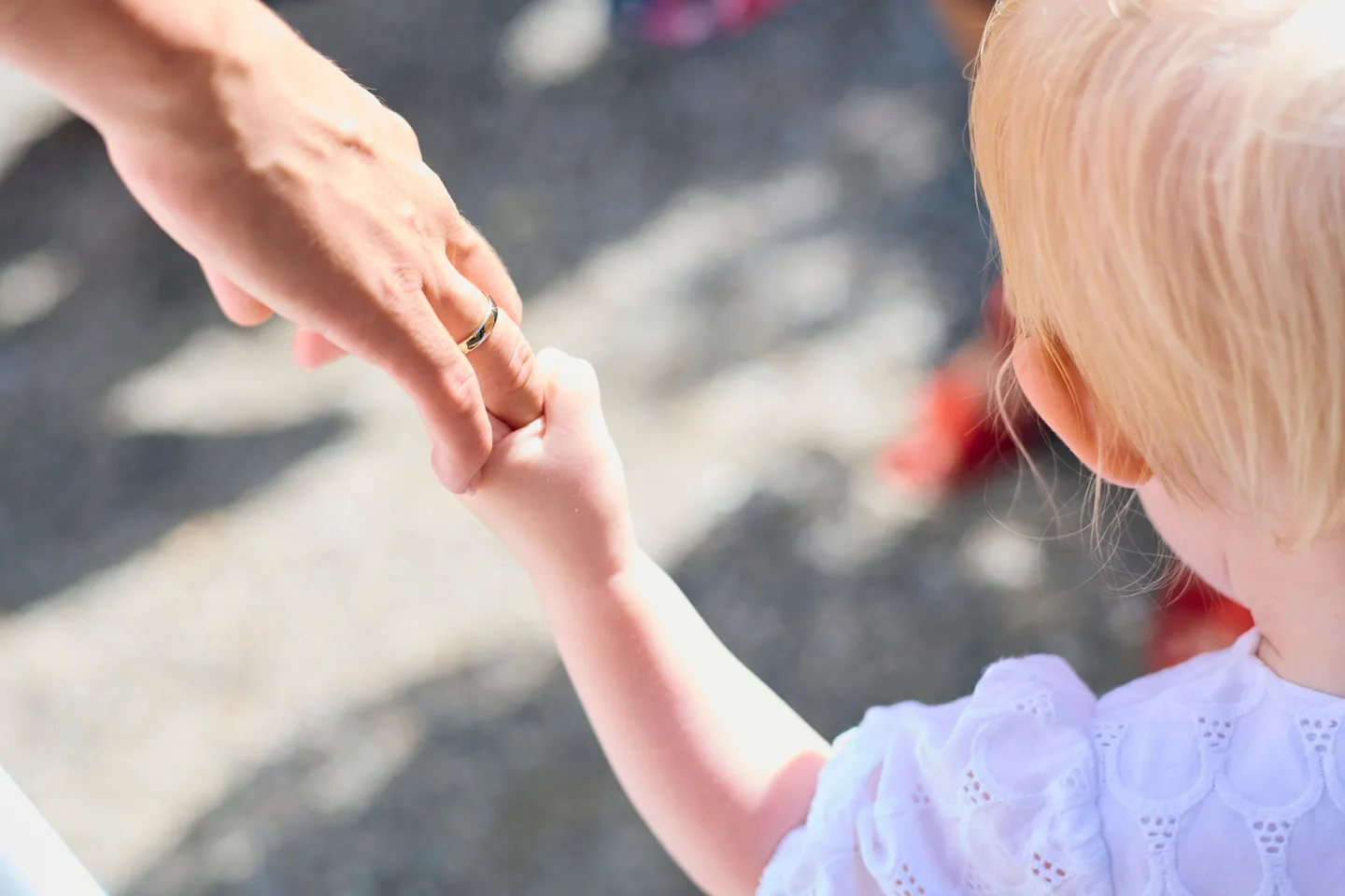 A young child holds a parent’s hand outdoors in warm sunlight.
